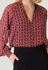 Langærmet bluse i gennemsigtig stof med et geometrisk mønster i pink, lilla og guld, med V-hals og knaplukning.
