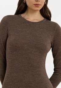 Bruine lange mouwen top in een zachte, gestructureerde stof met een ronde hals, voorzien van een getailleerd silhouet en minimalistische ontwerpdétails.