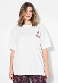 Bílý bavlněný tričko s krátkými, oversized rukávy. Na levé straně hrudi se nachází barevná grafika slunce a palmového stromu.