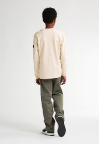 Beige langemouw t-shirt met geribde manchetten, gecombineerd met losse olijfgroene broek en zwarte sneakers met witte accenten.