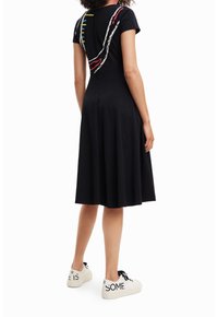 Černé šaty ke kolenům s krátkými rukávy, zdobené barevným vyšíváním ve vlnitém vzoru na zadní části. Nalezené s bílými teniskami.