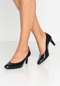 Černé lakované lodičky s embosovaným vzorem krokodýla, zaoblenou špičkou, otevřenou patou a 7 cm stiletto podpatkem.