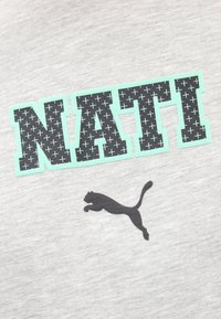 Κείμενο "NATI" με μαύρα σχέδια σταυρού, περιβαλλόμενο από ανοιχτό γαλάζιο περίγραμμα, πάνω από λογότυπο μαύρης πάνθηρας σε άλμα σε φόν ύφασμα ανοιχτού γκρι χρώματος.