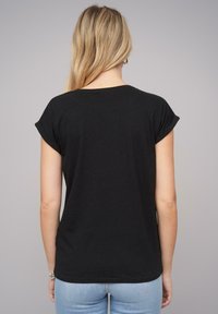 Juodas trumpomis rankovėmis T-shirt, pagamintas iš medvilnės, su laisvu siluetu ir suktomis briaunomis, derinamas su šviesiai mėlynomis džinsomis.
