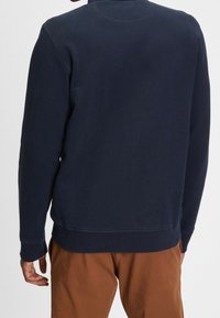 Námořnická modrá mikina s kulatým výstřihem, žebrovanými manžetami a lemem, a hladkým povrchem. Zadní strana má čistý, minimalistický design.