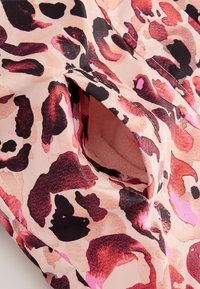 Gemustertes Gewebe mit einem pink-schwarzen Leopardenmuster und einer weichen Struktur. Das Design enthält eine Öffnung, in der ein Fleece-Futter sichtbar ist.