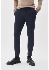 Marinblå skräddarsydda byxor i ett slätt tyg, med en slim fit, sidofickor och en rullad fåll. Matchas med svarta loafers.