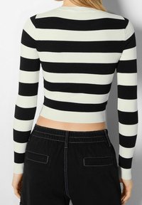 Pull cintré à rayures noires et blanches avec manches longues, texture côtelée, encolure ronde et coupe courte. Associé à un pantalon noir.