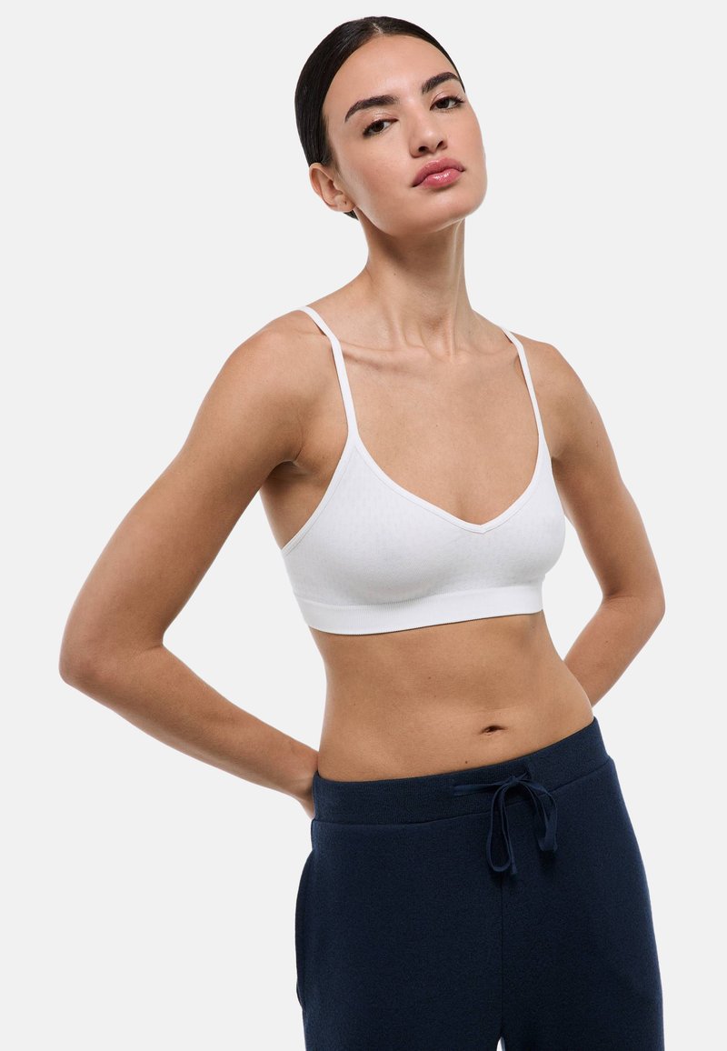 Bralette blanche sans fil avec des bretelles fines, un tissu texturé et un décolleté en V profond. Associé à un pantalon en toile bleu marine avec cordon de serrage.