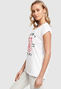 Hvid bomulds T-shirt med opfoldede ærmer, der har et rødt grafisk motiv af en kat og en ramen skål, med japansk tekst trykt nedenfor.