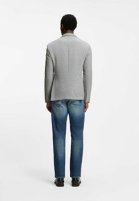 Grijze blazer met gestructureerde schouders en een enkel knoopsluiting, gecombineerd met lichtblauwe denim jeans, gezien van achteren.