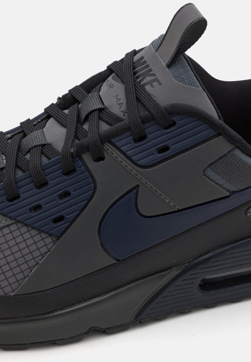 Baskets Nike Air Max, présentant un design texturé noir et navy, avec une semelle rembourrée, des lacets entrecroisés et un détail de logo proéminent.