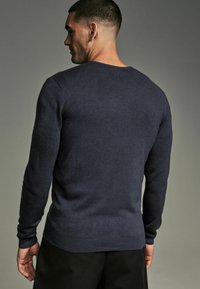 Pulover din lână navy cu mâneci lungi și guler rotund. Textură netedă și manșete și tiv ribbate, prezentat din spate.