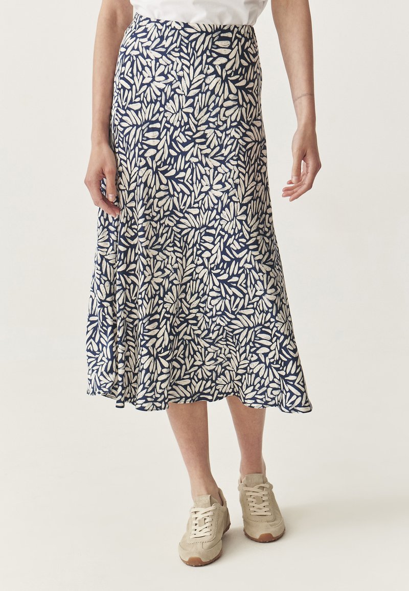 Jupe marine avec un imprimé de feuilles blanches, silhouette évasée, tissu doux et longueur mi-mollet, associée à des baskets beiges.