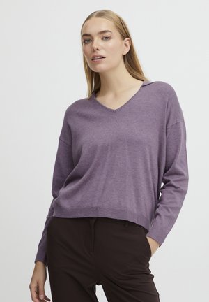 Lila V-Ausschnitt Pullover mit langen Ärmeln, aus weichem Strickmaterial gefertigt. Verfügt über eine lockere Passform und glatte Textur. Getragen über dunklen Hosen.