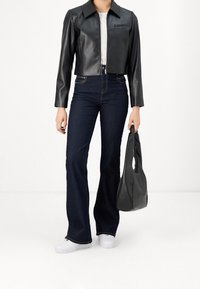 Kraftigt svart läderjacka med lång ärm, högmidjade mörkblå utsvängda jeans, vita sneakers och en svart handväska.