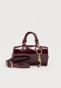 Petit sac à main en cuir verni bordeaux avec deux poignées supérieures, une bandoulière amovible et un accent de chaîne dorée avec un charme. Texture lisse et brillante.