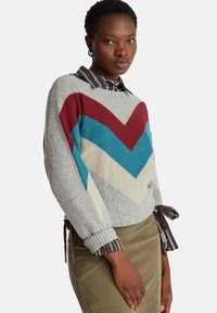 Svetle šedý svetr s chevronovým vzorem v barvách bordó, petrolejové a krémové. Obsahuje detaily pruhovaných stuh na rukávech a lemu.
