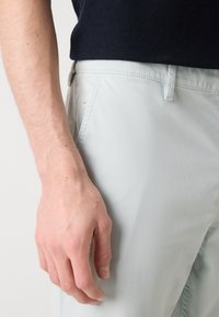 Pantaloni de culoare albastru deschis cu o finisare netedă, texturată. Prezintă un brâu standard și o buzunar lateral, cu cusături și detalii vizibile.