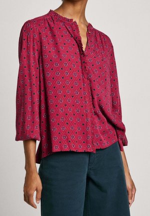Rood gebloemde blouse met een halslijn zonder kraag, opgehaalde schouders en driekwartmouwen. Heeft kleine cirkelvormige patronen in donkerblauw.