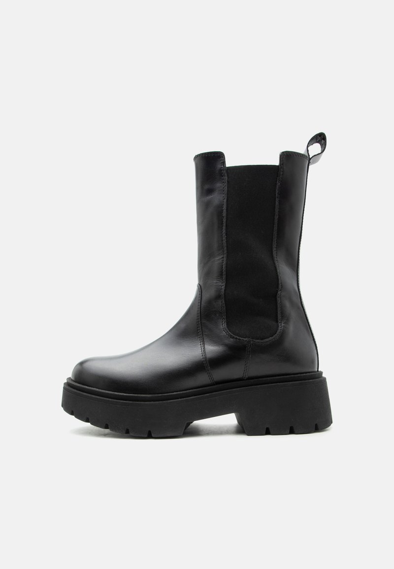 Bottine en cuir noir avec semelle épaisse, panneau latéral élastique et languette de traction sur fond blanc.