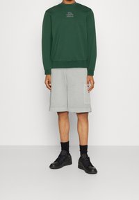 Sweat-shirt vert à col rond, short gris avec poches latérales et baskets noires, doté de poignets élastiques et d'une coupe décontractée.