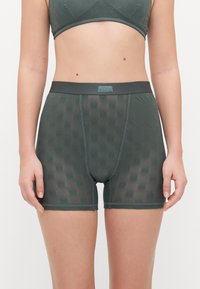Boxer shorts en maille verte avec des motifs floraux, taille élastique et jambes courtes. Le matériau est léger et a une texture douce.