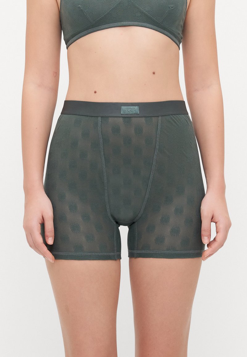 Boxer shorts en maille verte avec des motifs floraux, taille élastique et jambes courtes. Le matériau est léger et a une texture douce.
