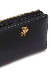 Μαύρο δερμάτινο πορτοφόλι με χρυσό λογότυπο, με φερμουάρ και αντίθετη ραφή, που αναδεικνύει μια λεία υφή με δομημένο σχήμα.