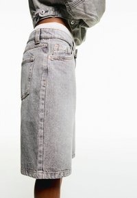 Gonna di denim grigia con design a vita media, tasche laterali e orlo grezzo. Il tessuto presenta un aspetto sbiadito e testurizzato.