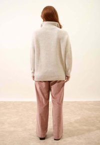 Maglione a coste di un grigio chiaro con colletto alto, abbinato a pantaloni in corduroy rosa chiaro e morbidi, a vestibilità ampia. Sfondo neutro.