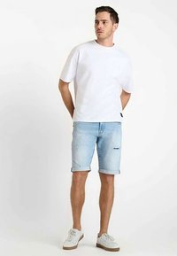 Camiseta blanca de algodón, de manga corta; pantalones cortos vaqueros azul claro con dobladillos remangados; zapatillas claras; diseño sencillo con marca sutil.