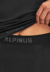 Czarne legginsy sportowe z teksturowanym pasem w kolorze czarnym, z logo marki "ALPINUS". Zbliżenie pokazuje gładki materiał oraz szczegółowe wzory szwów.