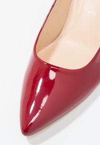 Chaussure à talon haut rouge brillant avec un bout pointu et un intérieur beige, marquée de la taille 4 1/2 à l'intérieur.