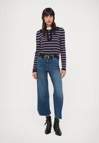 Temno modra majica z dolgimi rokavi s črtami v beli in roza barvi, okrašena z ovratnikom in gumbi; kombinirana z širokimi modrimi kavbojkami z visokim pasom.