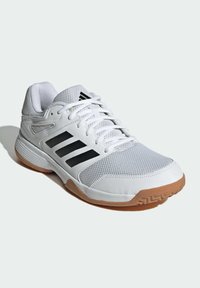 Zapatilla deportiva blanca con parte superior de malla transpirable, diseño de tres rayas negras y suela de goma. Presenta cordones y un cuello acolchado.