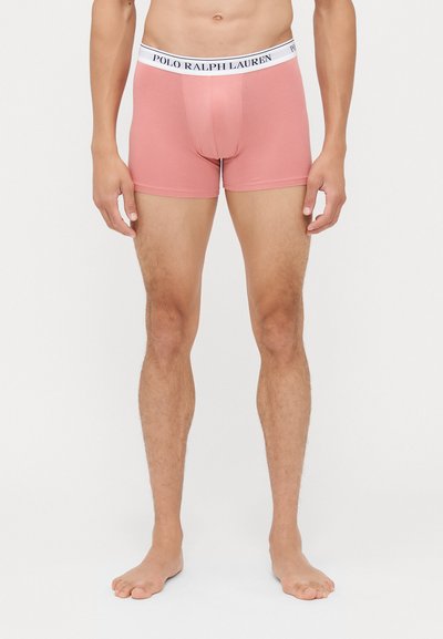 Moški bokserice iz svetlo roza tkanine, z belim pasom in mornarsko modrim logotipom "POLO RALPH LAUREN". Dolžina do sredine stegna, gladka tekstura.