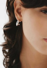 Pendientes de aro de plata con un diseño retorcido, que presentan superficies suaves y un acabado pulido. Forma curva con acentos sutiles.