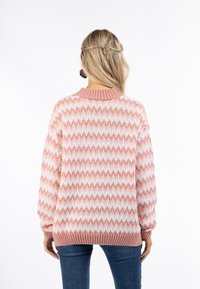 Rózsaszín és fehér zigzag mintás pulóver, laza szabású, bordázott kerek nyakkivágással és szegéllyel, texturált kötött anyagból készült, kék farmerral párosítva.