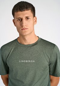 T-shirt verde a maniche corte realizzato in tessuto testurizzato, con la parola "LINDBERGH" stampata in bianco sul davanti. Semplice colletto a girocollo.