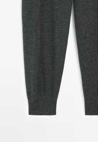 Donkergrijze gebreide sweater mouwen met geribbelde manchetten liggen plat op een witte ondergrond.