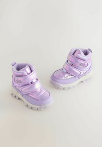 Lila Winterstiefel mit glänzenden, metallischen Akzenten, zwei Klettverschlüssen, einem gepolsterten Innenraum und einer strukturierten Gummisohle für besseren Halt.