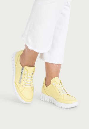 Person wearing light yellow sneakers with white soles and laces, paired with white cropped pants with frayed hems.