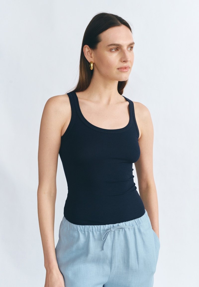 Granatowy top na ramiączkach w prążki o dopasowanym kroju i szerokich ramiączkach, w połączeniu z jasnoniebieskimi spodniami o luźnym kroju i elastycznym pasie.