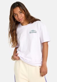 Biela bavlnená tričká s malým modro-zeleným logom "Billabong" na hrudi, uvoľnený strih a krátke rukávy.