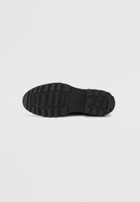 Suela de zapato de goma negra con patrones de relieve texturizados y una profunda tracción. Perfil plano y diseño de punta redondeada para mayor estabilidad.