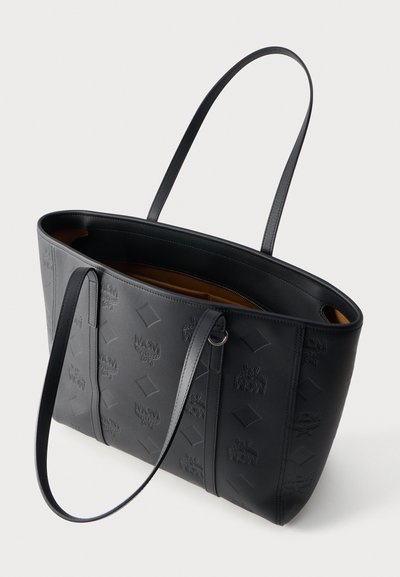 Sac cabas en cuir noir avec motif logo MCM embossé, intérieur couleur cognac, ouverture sur le dessus et deux longues bandoulières.