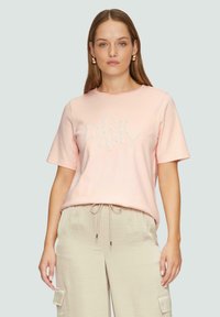 Różowa koszulka z krótkim rękawem, z napisem "DREAMY" haftowanym w teksturowanej czcionce. Okrągły dekolt, miękka tkanina, w zestawie z jasnobeżowymi spodniami.