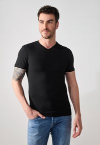 Tricou negru cu mânecă scurtă și decolteu în V. Materialul pare neted și ajustat, asortat cu blugi denim de o nuanță albastră deschisă.