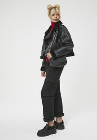 Czarna skórzana kurtka z krótkim krojem i futrzanym kołnierzem, czerwony golf, czarne teksturowane spodnie cargo oraz czarne buty na platformie. Torebka na ramię z logo.